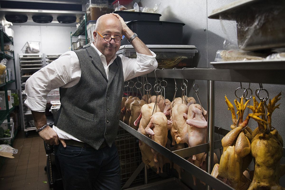 Andrew Zimmern poses in front of hanging ducks and chickens inside the kitchen at Lucky Cricket