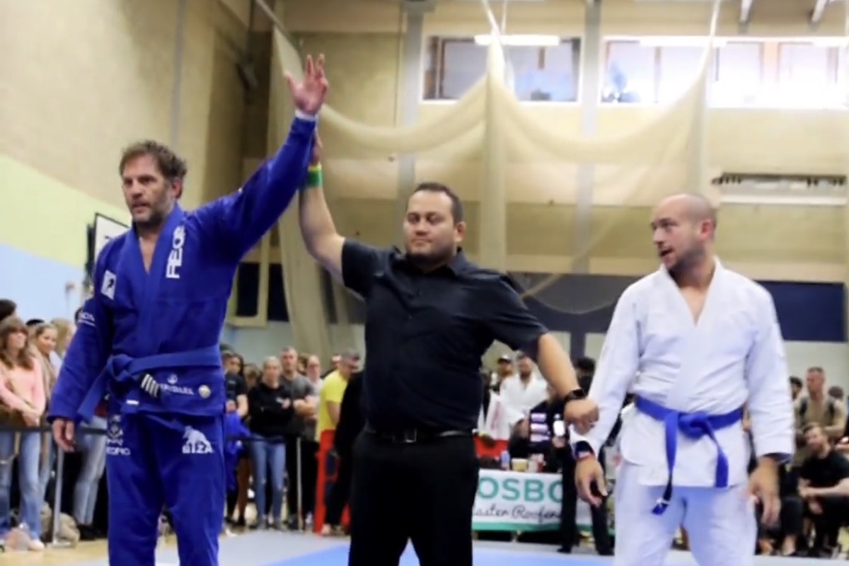 Tom Hardy getting his hand raised after submitting his opponent in a BJJ competition.