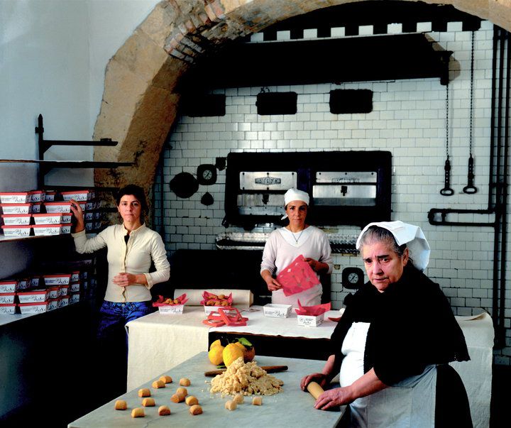 Three bakers perform various tasks in a large, tiled kitchen. 