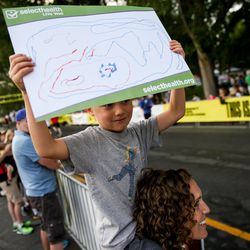 Jordan Steiner, 5, holds a homemade sign while sitting on the shoulder of his mother, Maylynn Steiner, and waiting to see his dad, Scott Steiner, finish running the Deseret News 10K at Liberty Park in Salt Lake City on Tuesday, July 24, 2018.