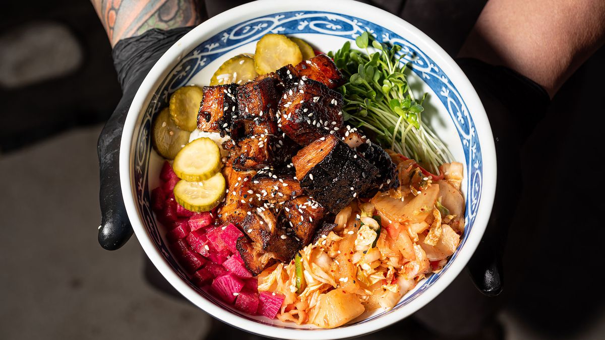 A blue and white bowl shows rice and pork belly and veggies and more.
