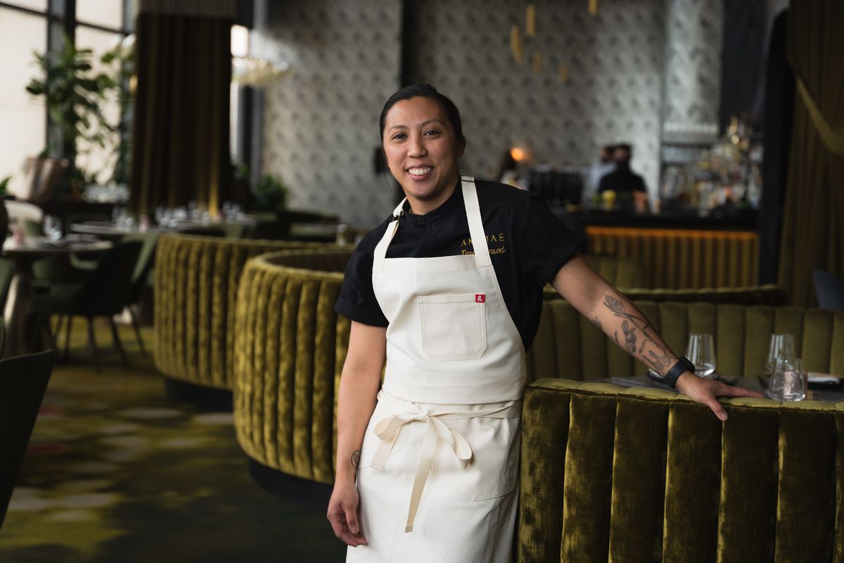 A woman in a chef’s apron stands in a fancy dining room.