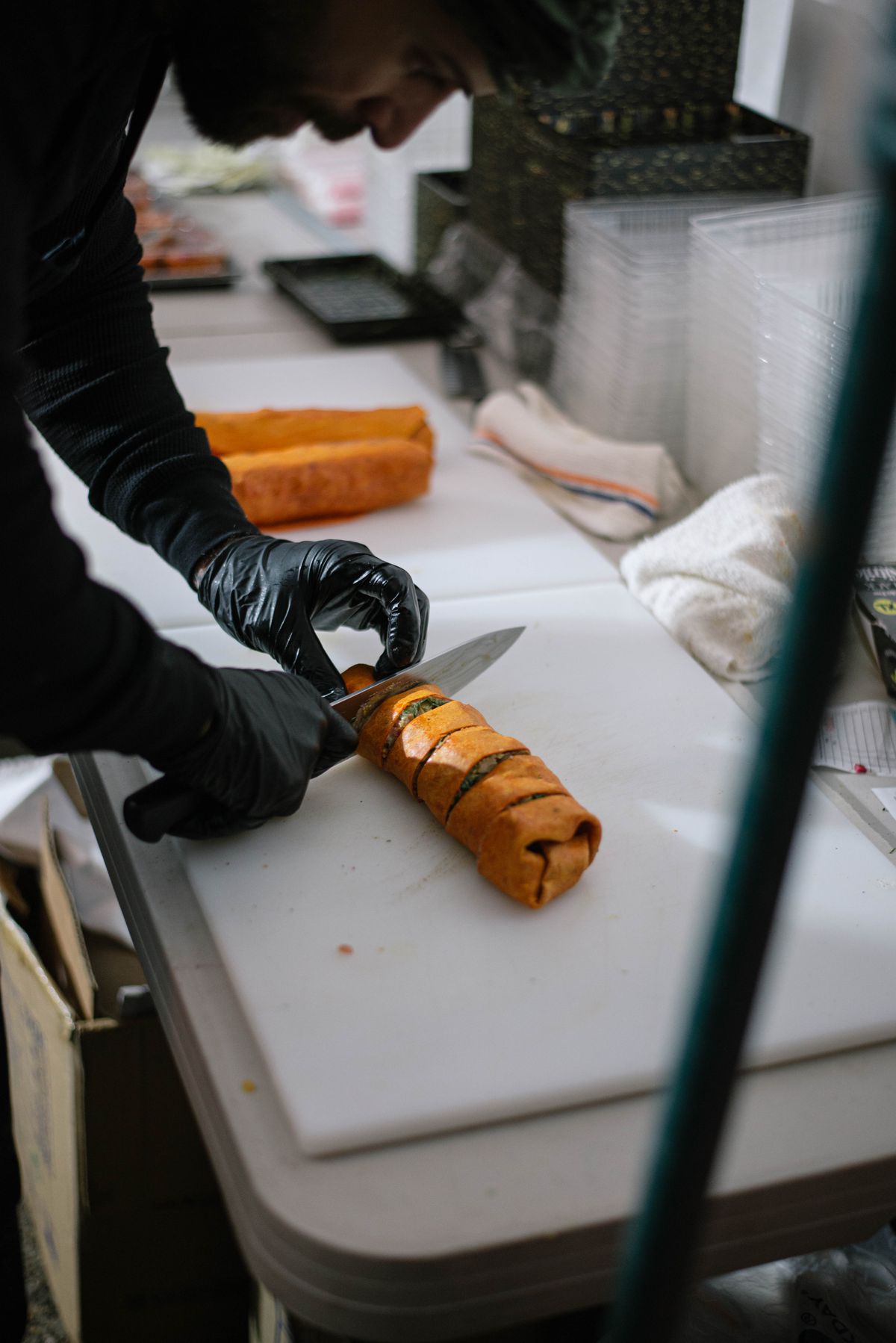 A man wearing black latex gloves slicing an orange wrapped stuffed with beef shawarma on a white cutting board