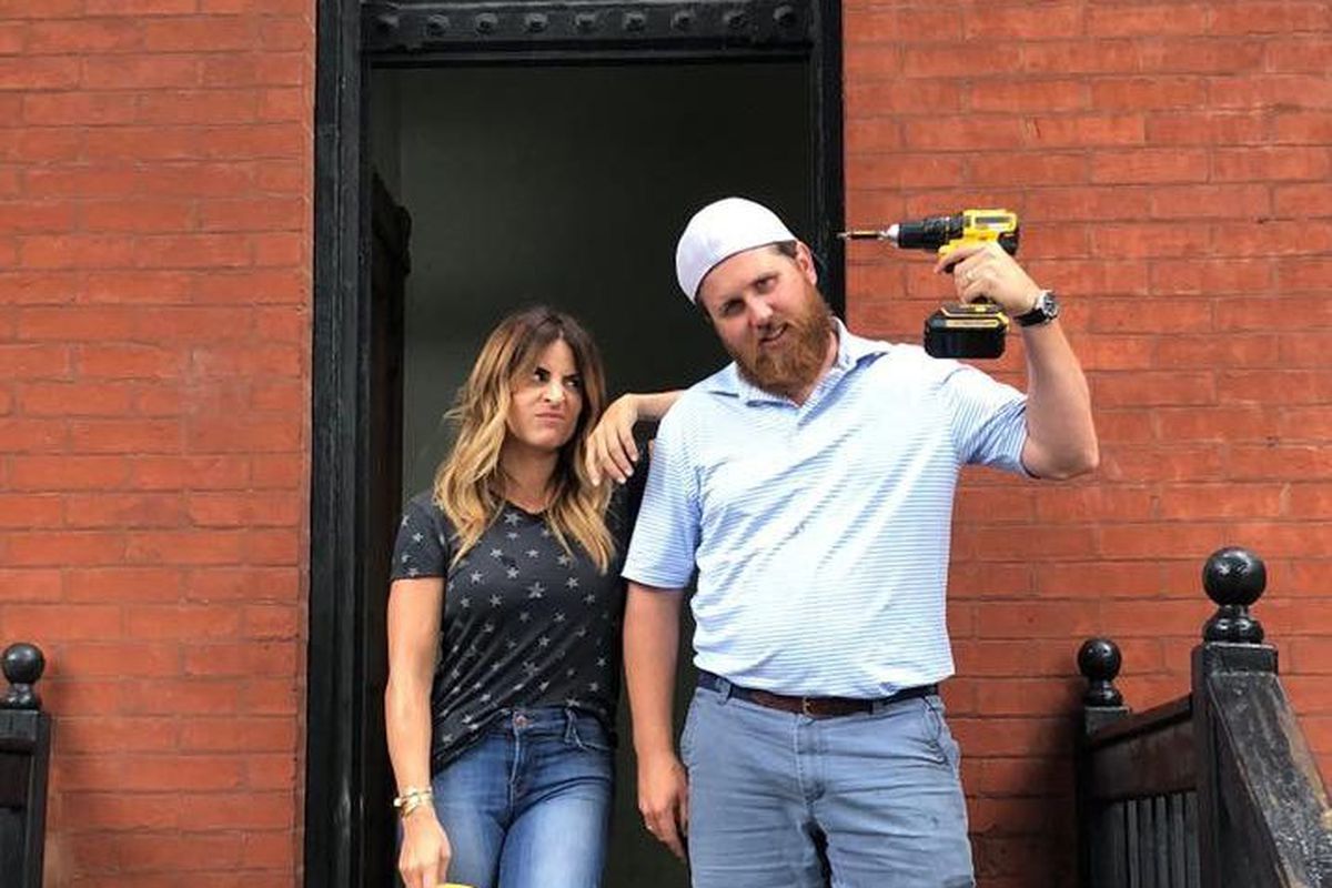 Donovan Eckhardt and Alison Victoria, the hosts of the TV show “Windy City Rehab,” are standing outside a city building and Eckhardt is holding a power drill.