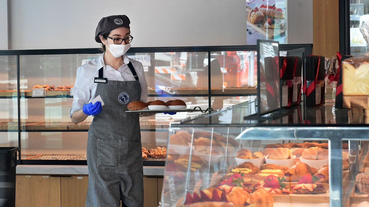 A restaurant worker wears a face mask and gloves and adds pastries into a pastry case.