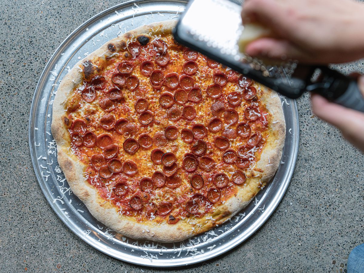 A hand grates parmesan over a pepperoni pizza at Pizza Thief in Portland, Oregon.