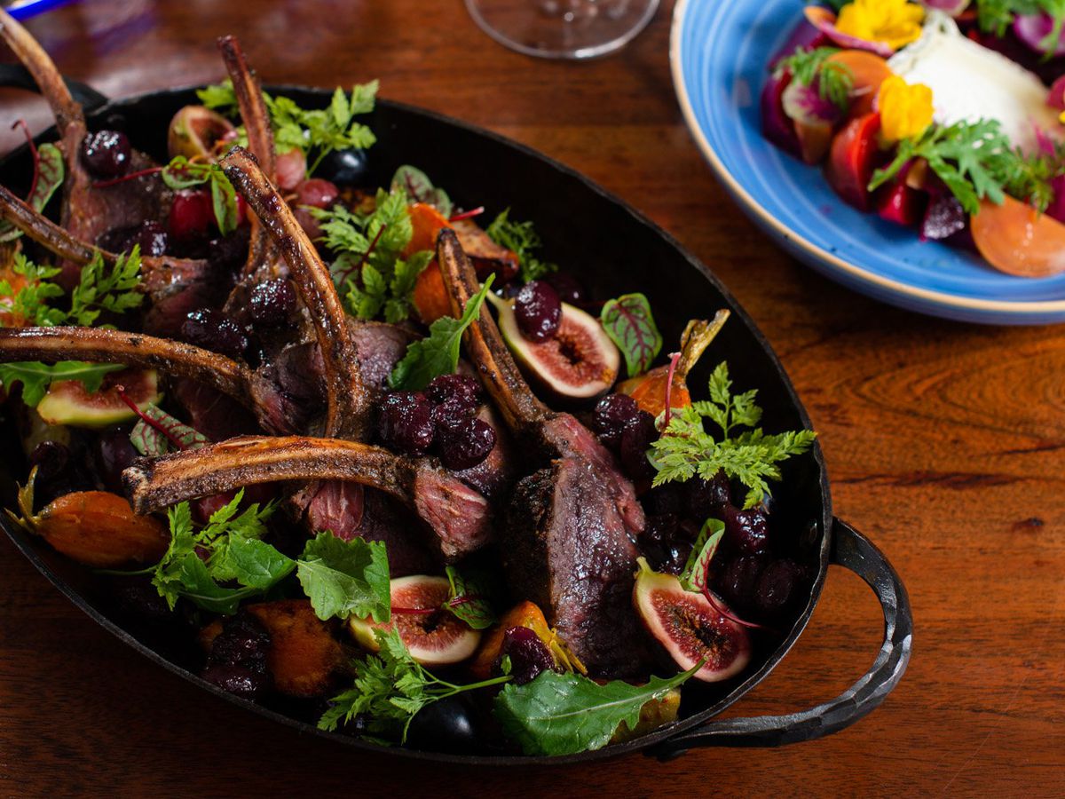 Lamb chops in a wide bowl with red wine on a wooden table.