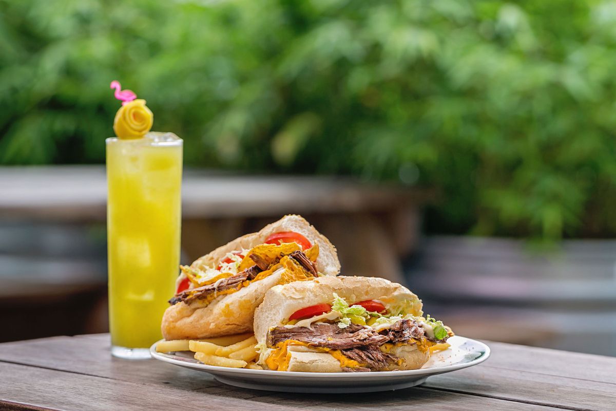 a beefy po’boy sandwich and a yellow cocktail with a lemon twist