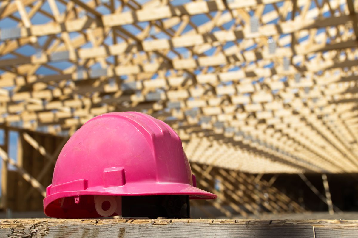 A pink safety helmet placed on a wooden sawhorse with wood framing trusses in background.