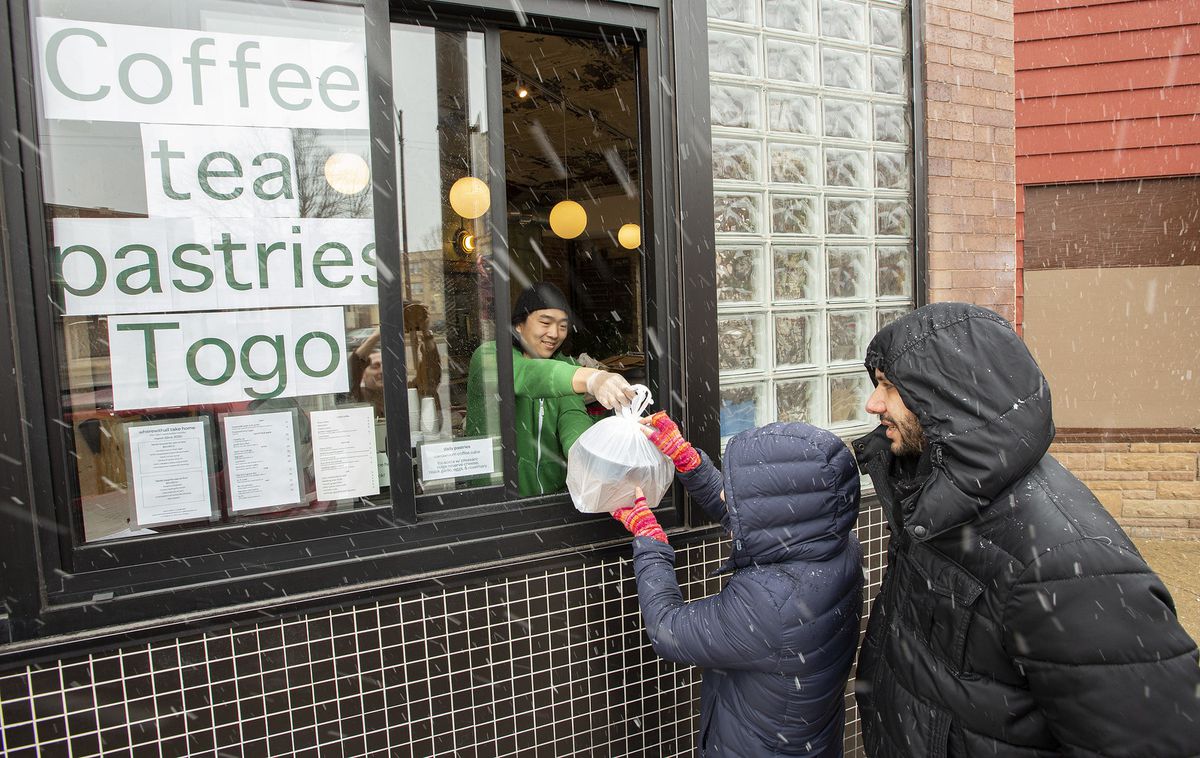 A person hands a bag through a window to a child in the falling snow with a parent watching.