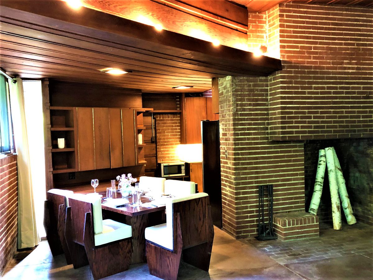 A dining room table with six chairs and cushions sits next to the brick fireplace.