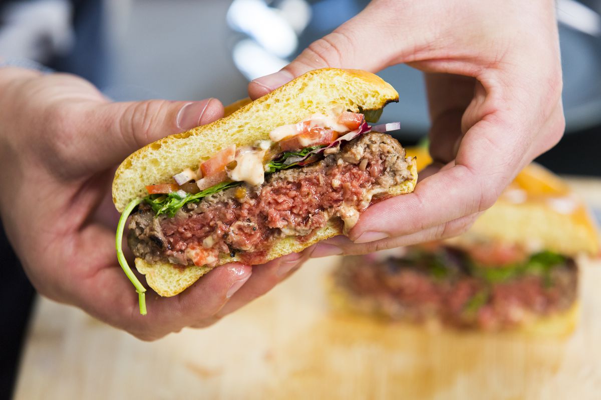 An Impossible burger cut half open and in a person’s hands.
