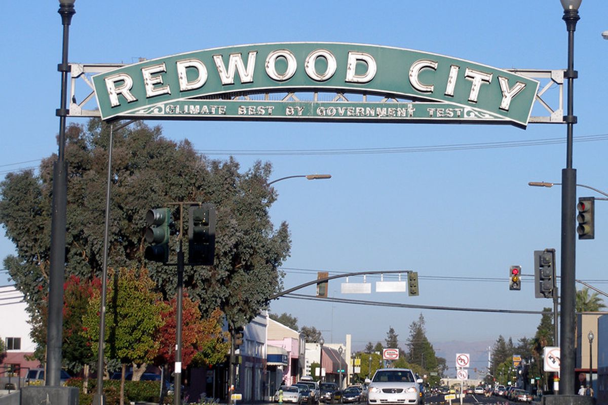 A sign above a street. The sign has these words on it: Redwood City.