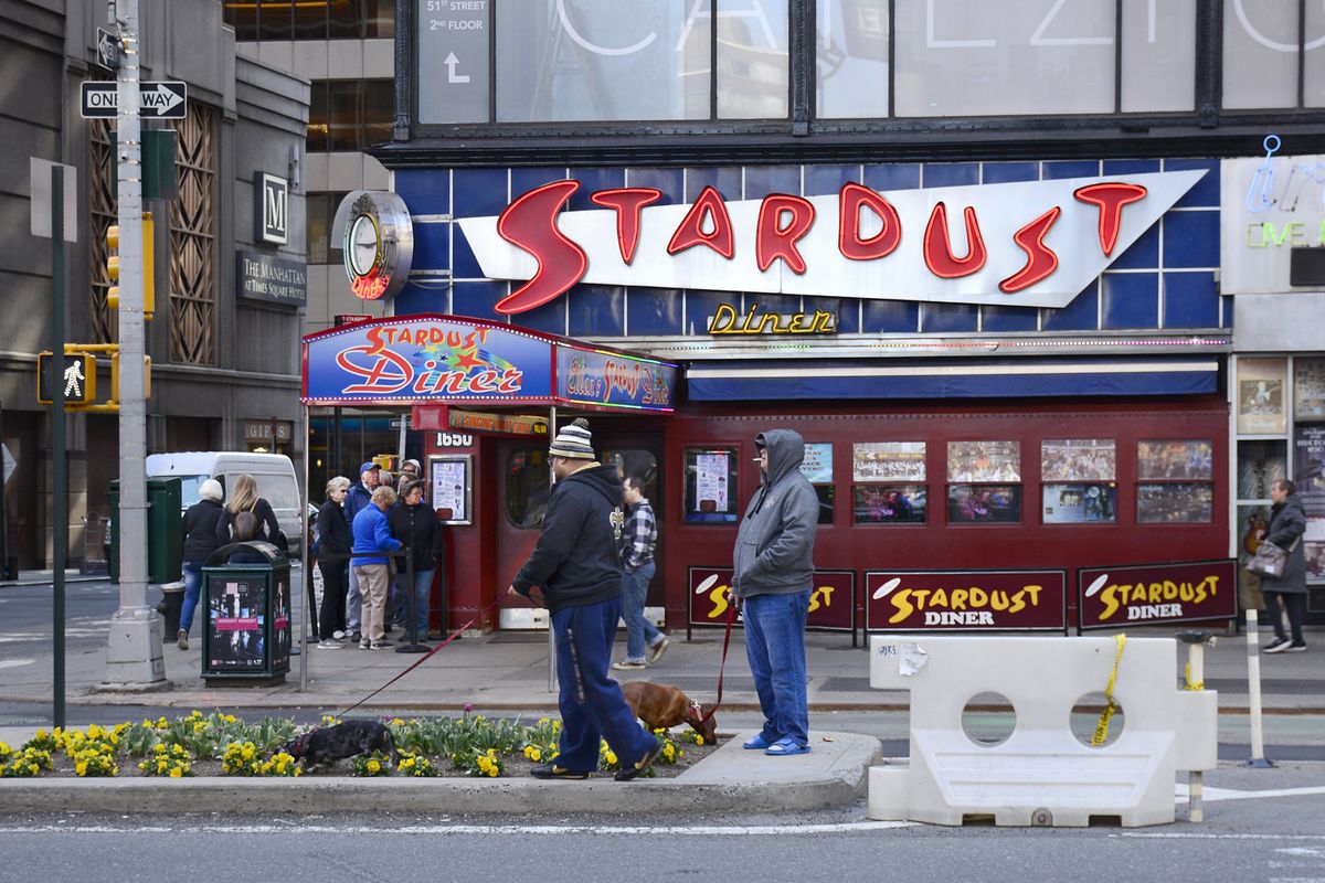 Two men walk their dogs in a flower bed as customers line up to enter the 1950s-themed Ellen’s Stardust Diner on Broadway in New York City’s Theater District.