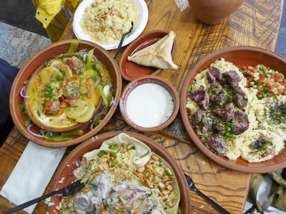 Several shallow brown clay dishes with rice, kebabs, a yellow stew, with bright white yogurt sauce in the middle.