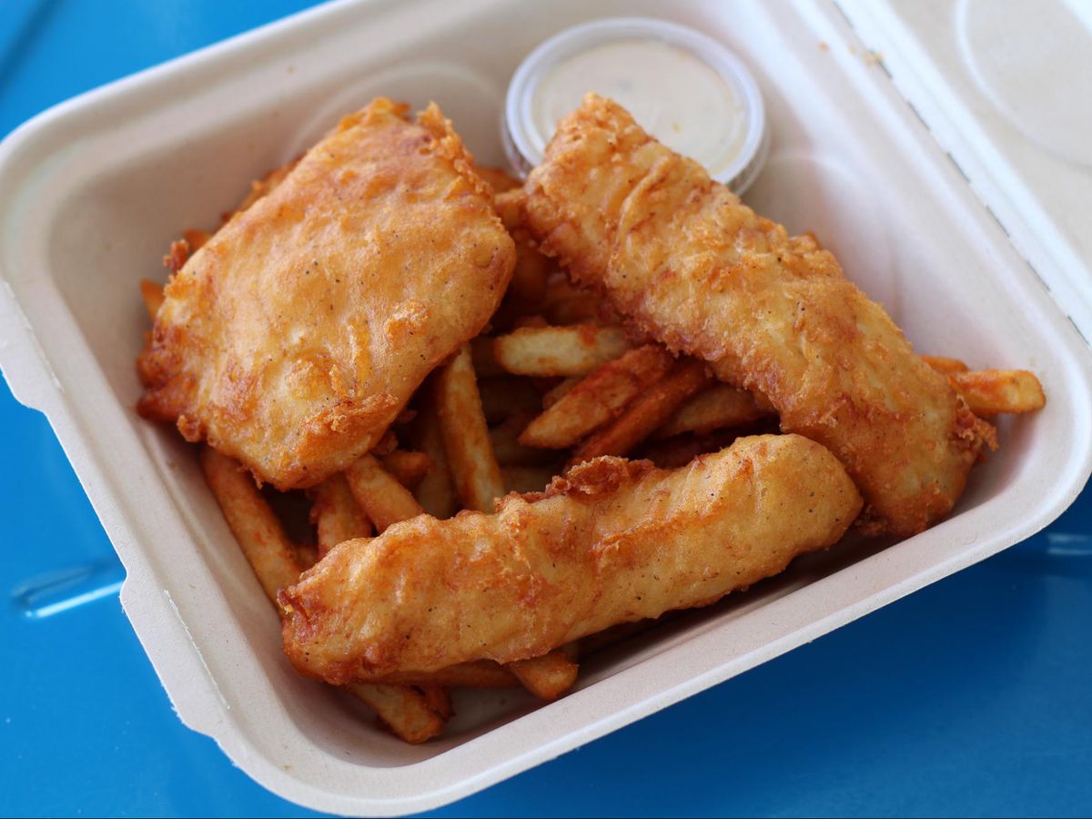 Three pieces of beer-battered halibut with fries in a paper takeout container.
