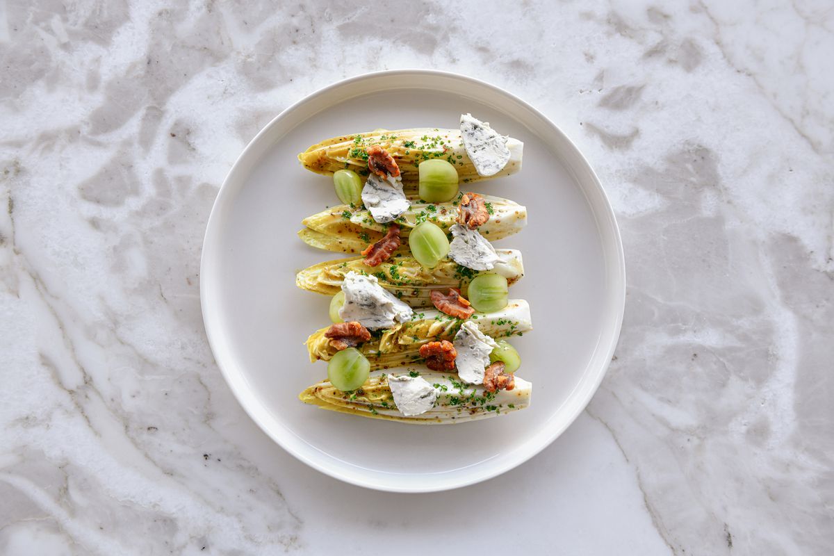An overhead shot of four lines of endive with creme fraiche on a marble table.