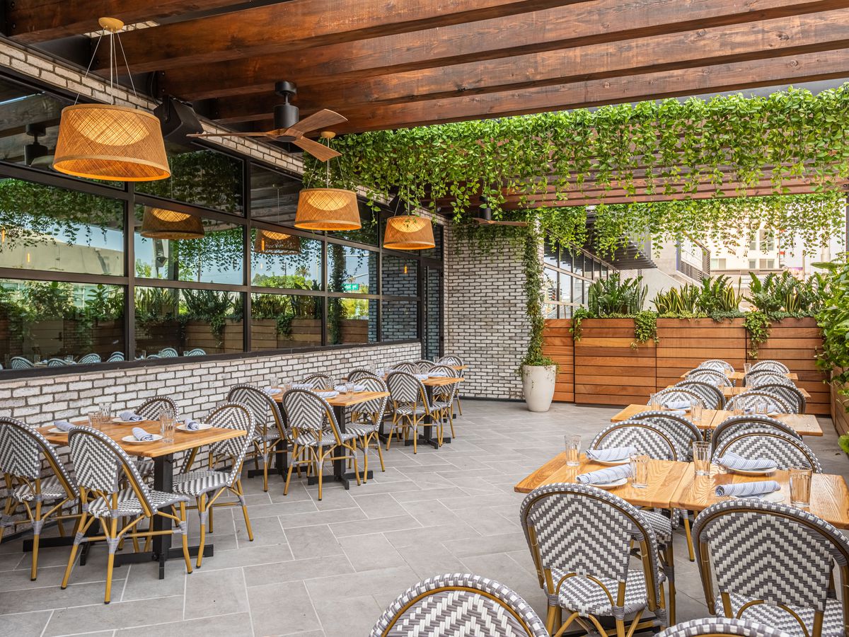 One side of a patio at a restaurant with cafe woven chairs and wooden tables.