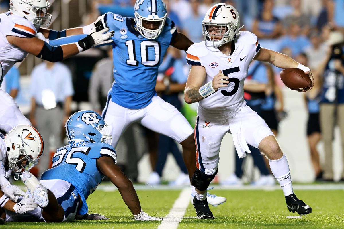 Brennan Armstrong #5 of the Virginia Cavaliers rolls out under pressure from Kaimon Rucker #25 and Desmond Evans #10 of the North Carolina Tar Heels during the first half of their game at Kenan Memorial Stadium on September 18, 2021 in Chapel Hill, North Carolina.