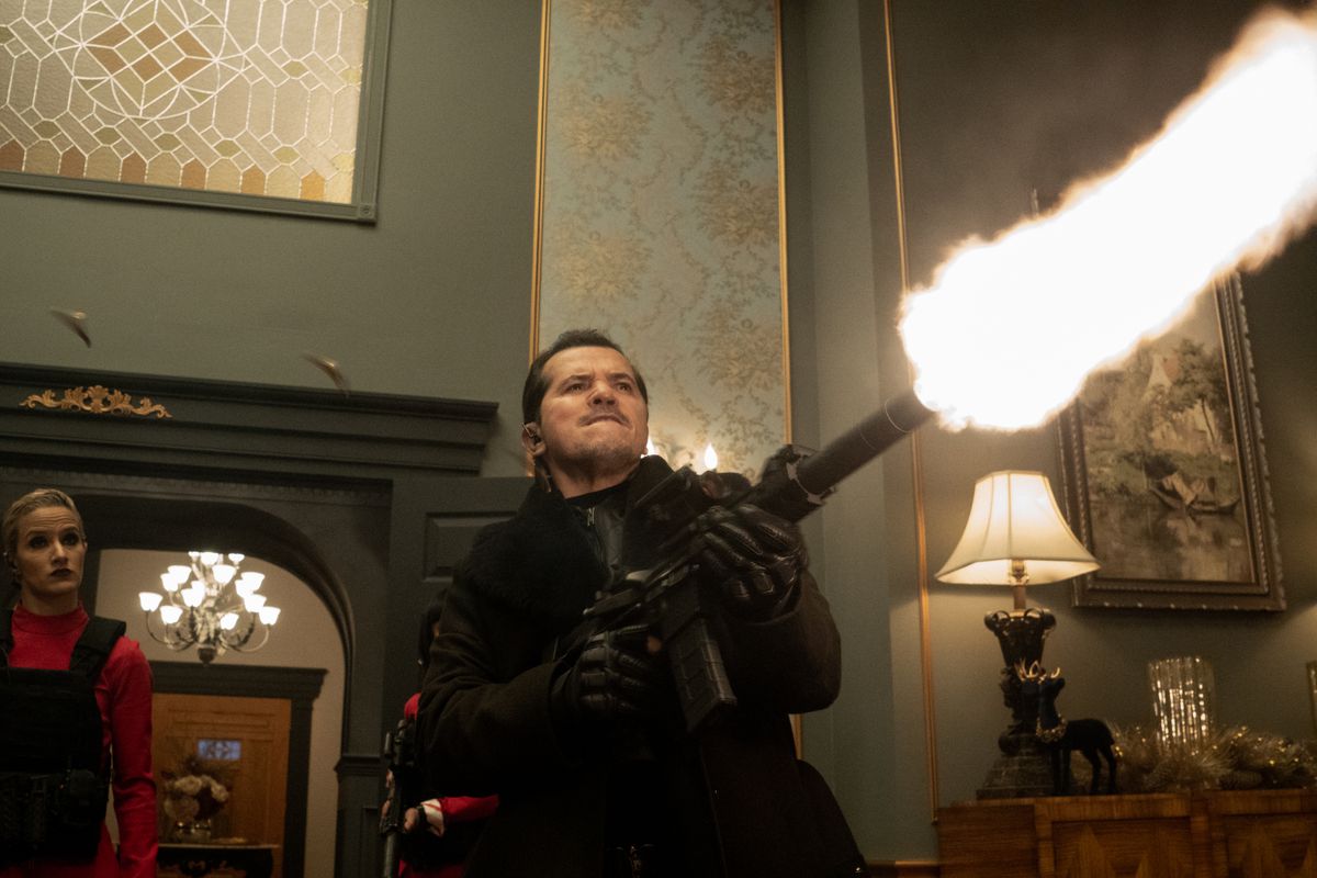 Scrooge (John Leguizamo) grimaces and fires an automatic rifle into the air with a huge muzzle flash in what looks like a scene from Scarface, but it’s actually from Violent Night