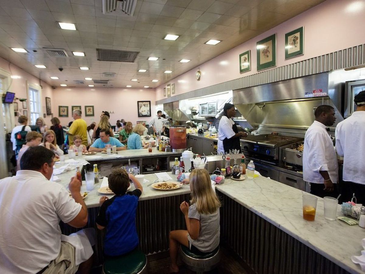 Kids and adults dine at the counter in a restaurant in front of an open kitchen.