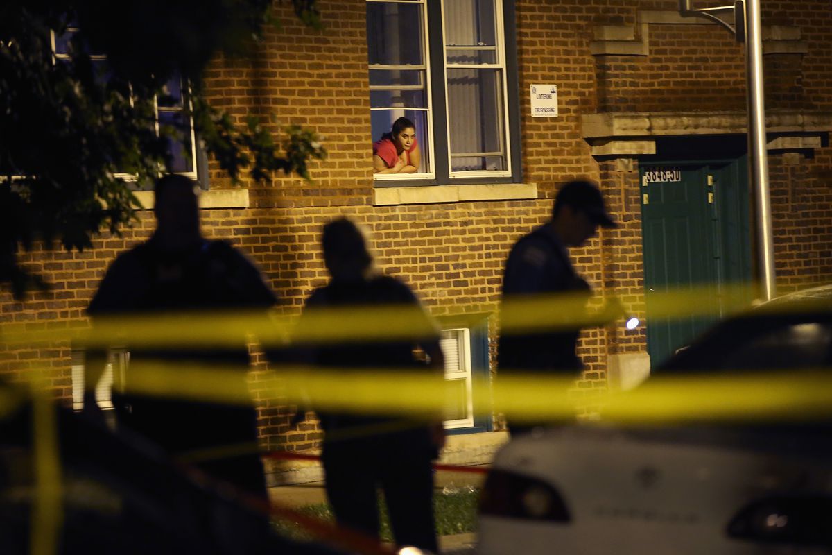 A woman watches from her window as police look for evidence at a Chicago crime scene.