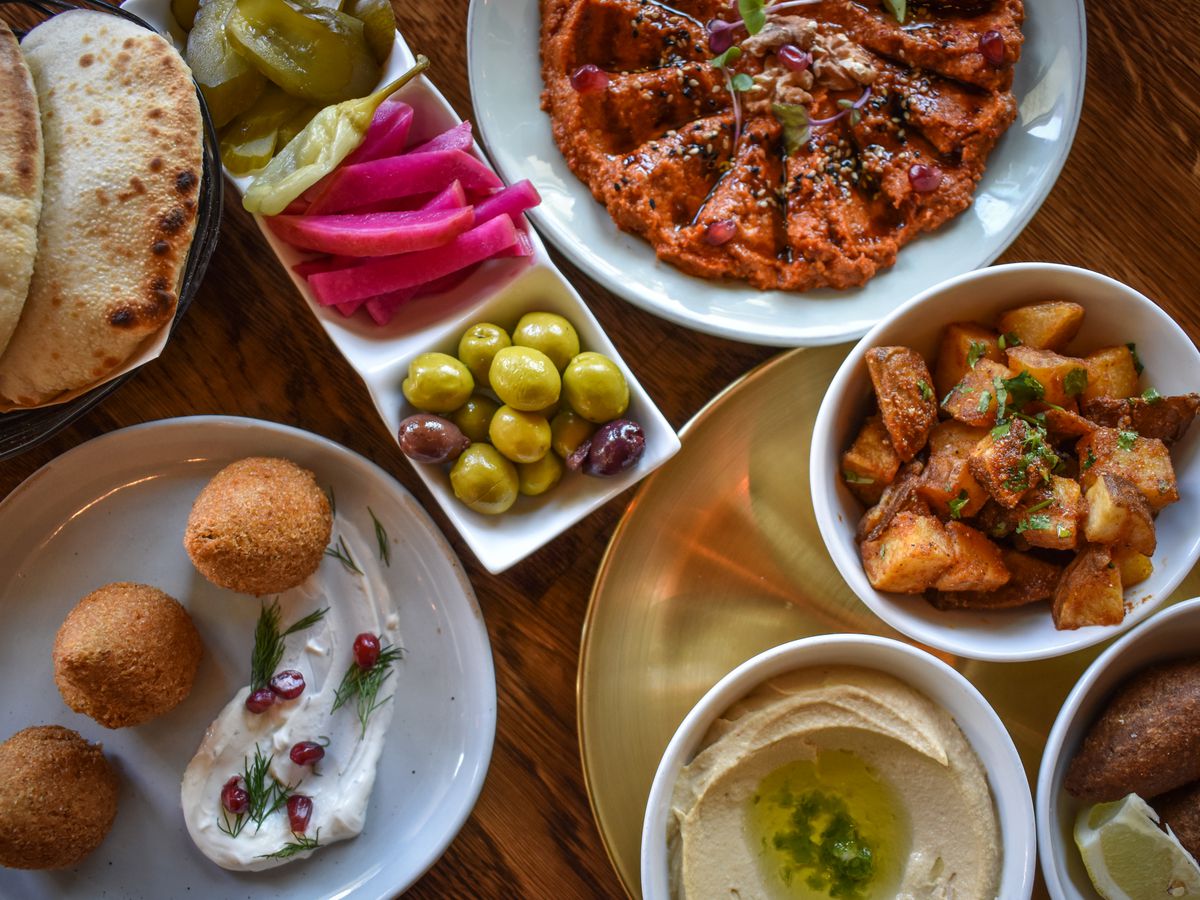 Seven Middle Eastern dishes like kibbe and hummus on display at a table at Ammatolí.