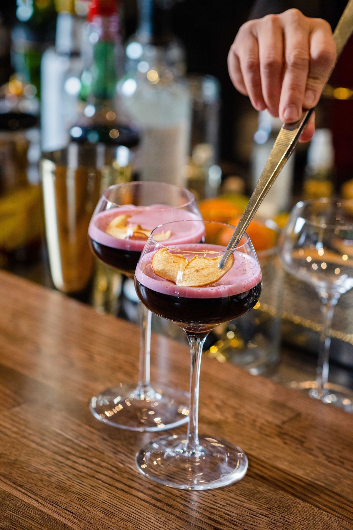 A bartender places a dried apple garnish on top of a purple cocktail.