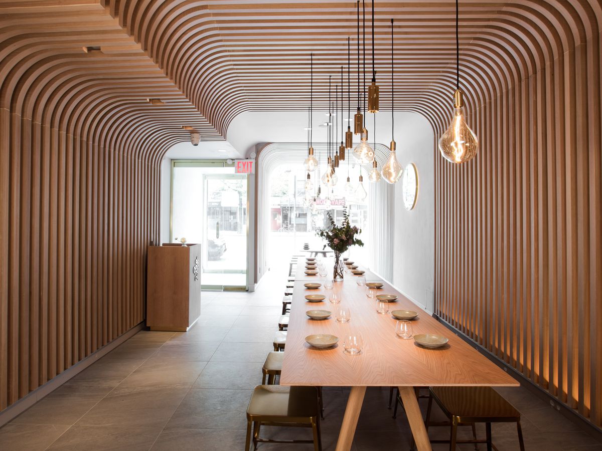 An artistic dining room with blonde wood slats from floor to ceiling and hanging exposed bulb lights