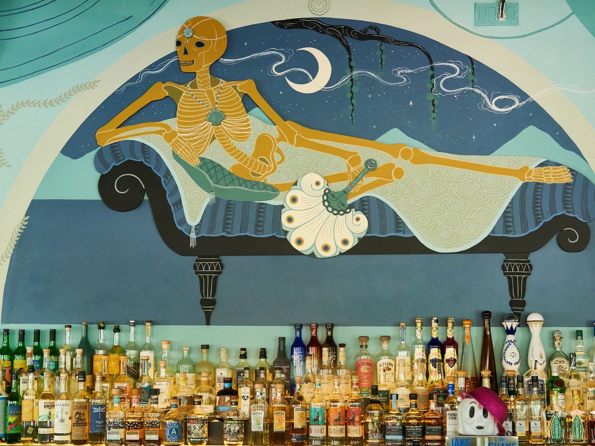 An art deco style mural of a reposing skeleton behind a well-stocked bar.