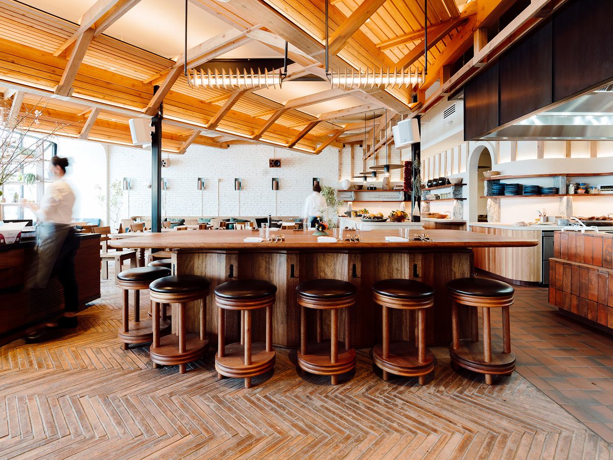 A rounded wood bar surrounded by stools in an airy, sunny restaurant. 