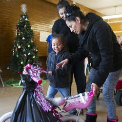 Camila Mendoza, 4, smiles as her mom, Georgina Errguin, shows her a new bike she received during Operation Chimney Drop at James R. Russell Head Start in Salt Lake City on Friday, Dec. 16, 2016. Each year, Utah Community Action pairs donors with low-income families. Donors then purchase holiday gifts that are then distributed by Utah Community Action’s staff. Donated items this year included  winter coats, hats and scarves, clothing and shoes, toys, hygiene essentials, nonperishable and canned food items, books and more.