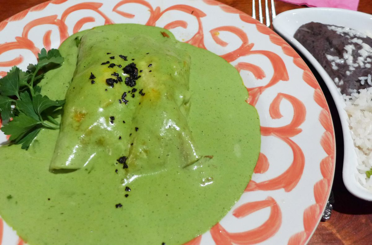 Two enchiladas smothered in green sauce on a patterned orange plate.
