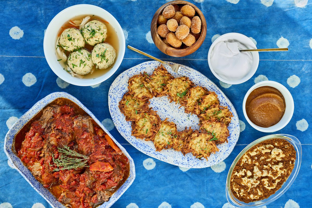 A spotted blue tablecloth topped with Hanukkah platters like golden-fried latkes, powdered brioche doughnut holes, and onion-braised brisket.