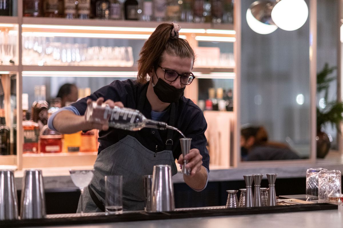 A bartender with a ponytail pours alcohol.