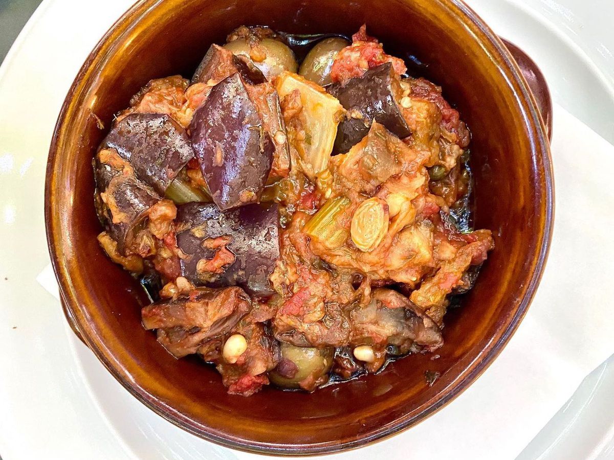 From above, a glazed clay bowl containing bright caponata, with especially vibrant purple eggplant