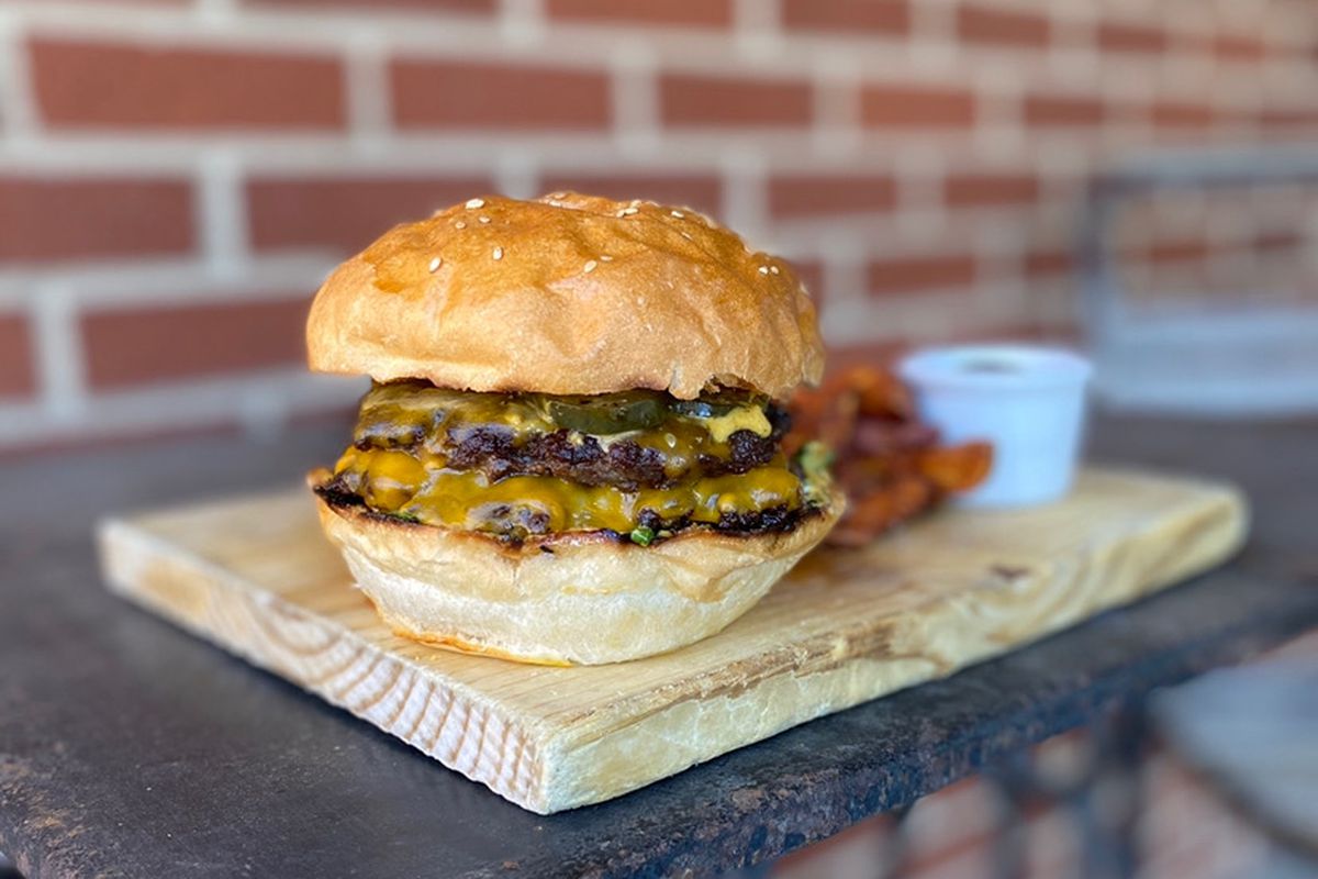 A double cheeseburger on a wooden slab in front of a brick wall