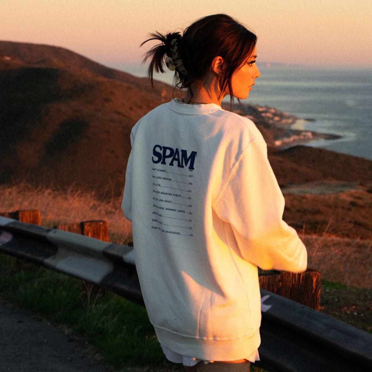 A woman wearing a Spam sweatshirt and staring off into the sunset