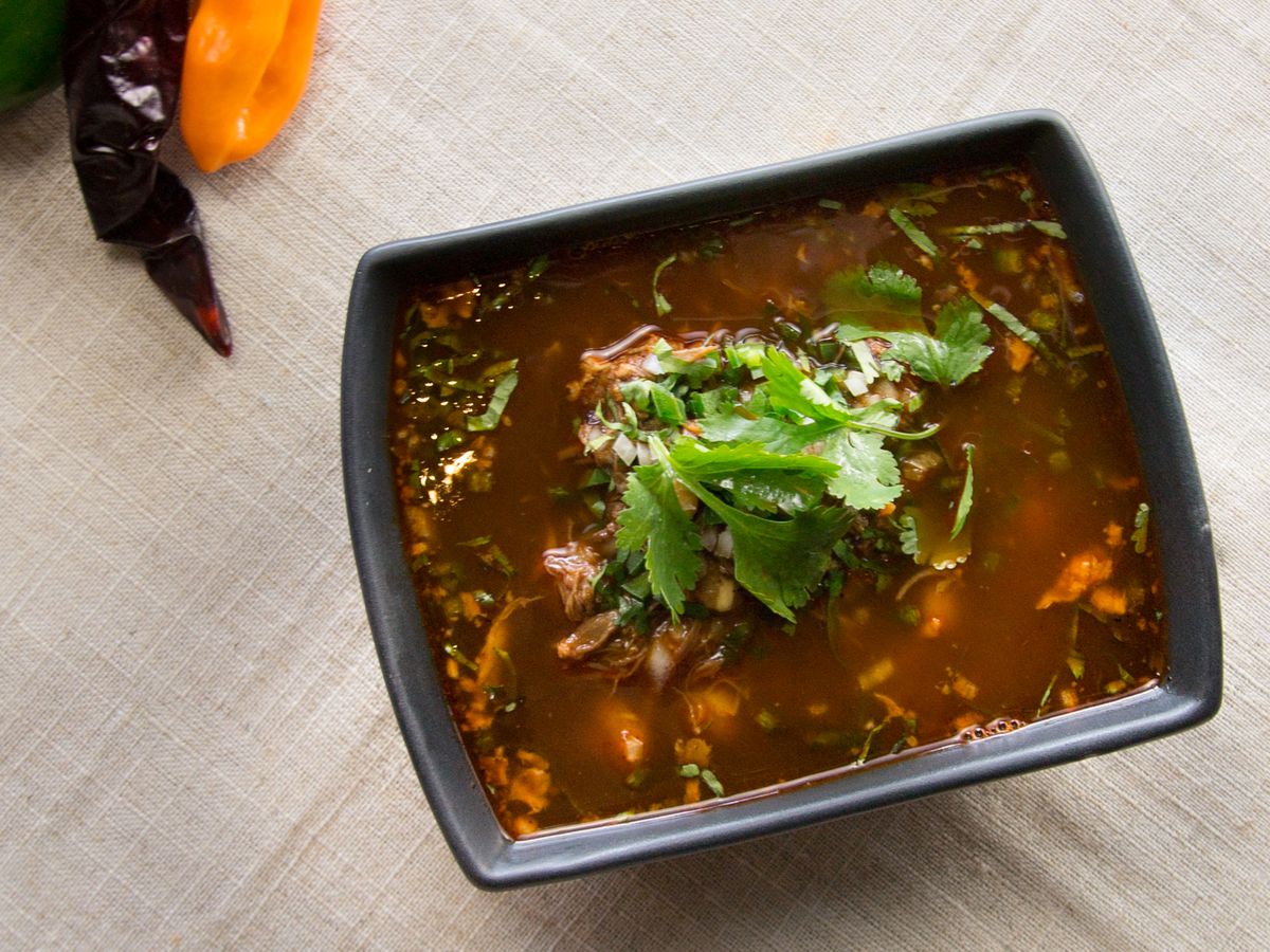A black square-ish bowl filled with a red-toned soup topped with cilantro. 