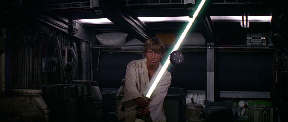 Luke Skywalker holds his lightsaber up against a practice drone in A New Hope.