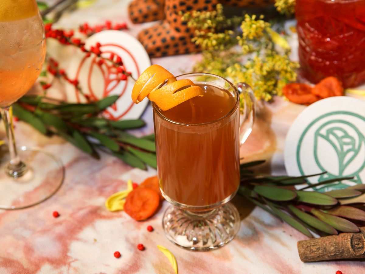 A mug of spiked cider sits on a table surrounded by garlands and holly.