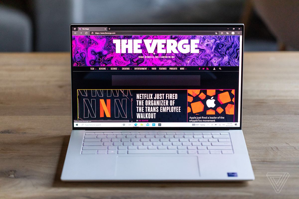 The Dell XPS 15 seen from the front on a wooden table. The screen displays The Verge homepage.