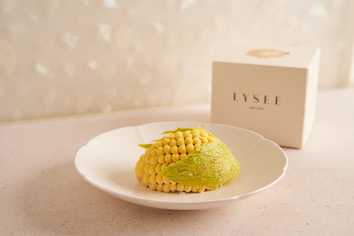 Un bol blanc contient un dessert rond qui ressemble à un épi de maïs.  En arrière-plan se dresse une boîte qui dit Lysée.