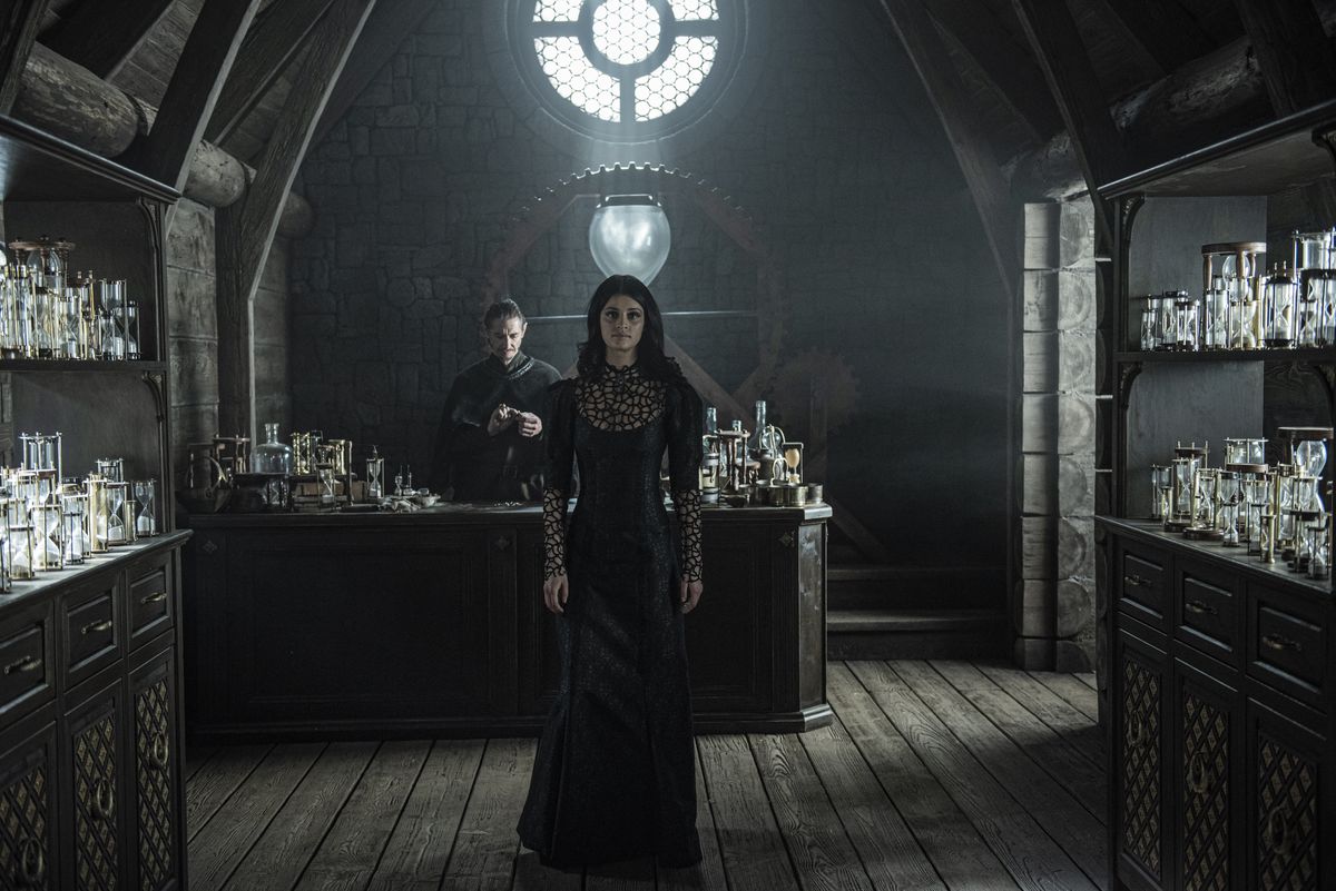 a dark-haired woman in a black dress walks between shelves of hourglasses in The Witcher