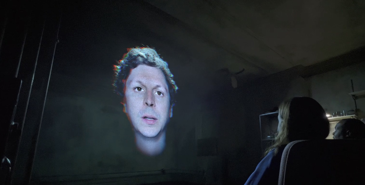 A CG rendering of Michael Cera floating in a basement as a woman sits on a couch watching to him talk