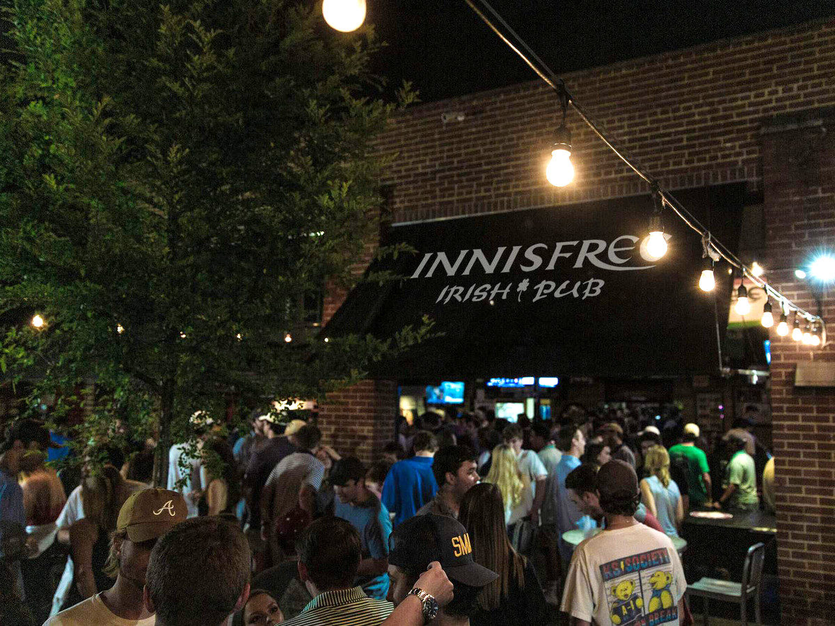 A crowd of young people on the patio of a redbrick pub where an awning reads Innisfree Irish Pub.