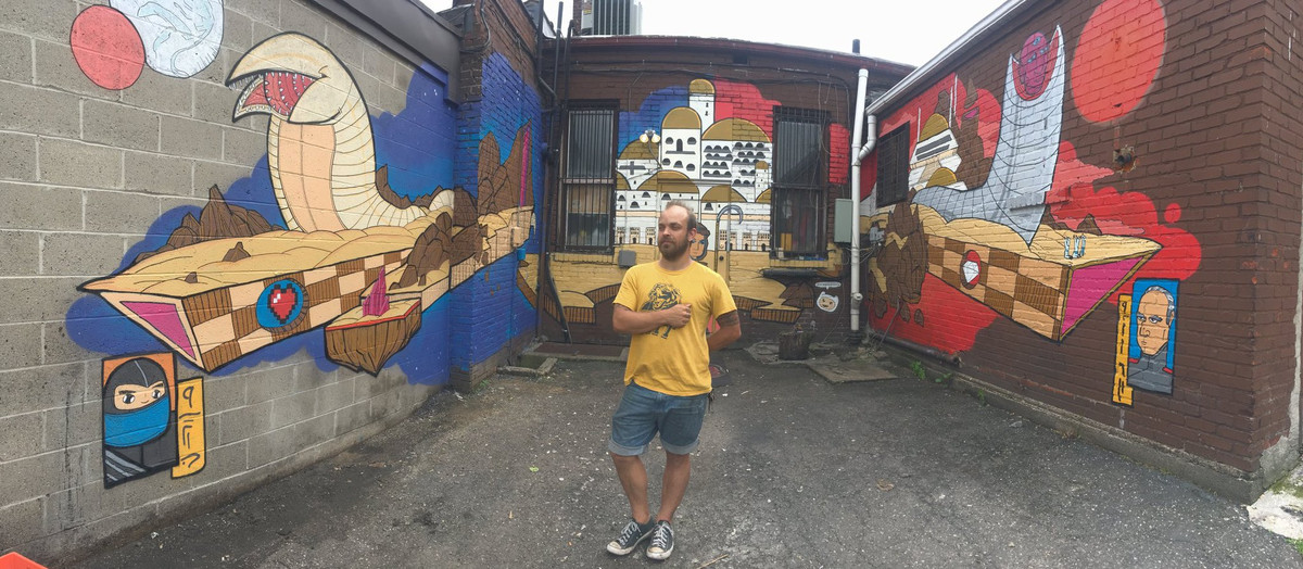 Mural artist Brian Gonnella standing in front of his Dune mural, behind Pizza Pronto