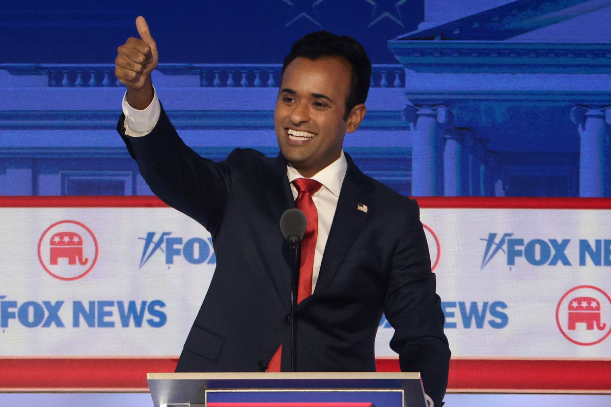 Vivek Ramaswamy waves to the audience from behind a podium, with Fox News banners behind him,