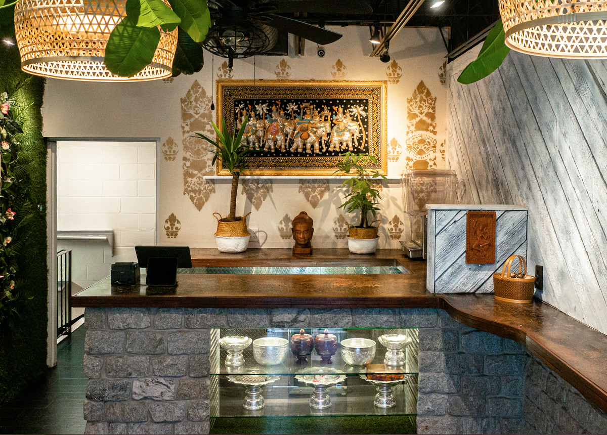 Interior of a small counter restaurant featuring Cambodian art and artefacts.  The counter is dark wood with decorative stone coating.
