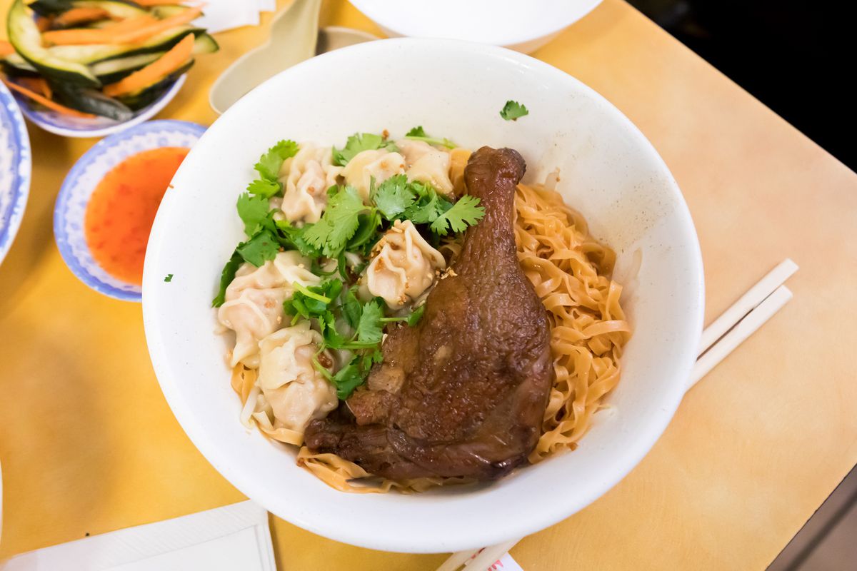 A bowl of noodles with wontons and a duck leg.